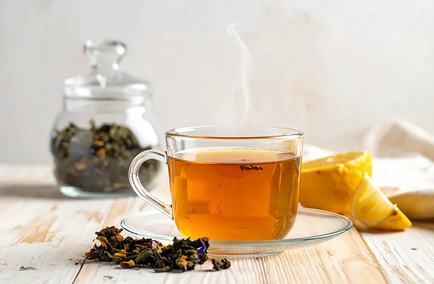 Tasse de tisane, tranches de citron, feuilles séchées dans un pot en verre.