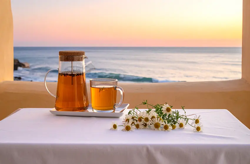 Tisanes posées sur une table avec nappe blanche et vue sur la mer avant d'aller dormir.